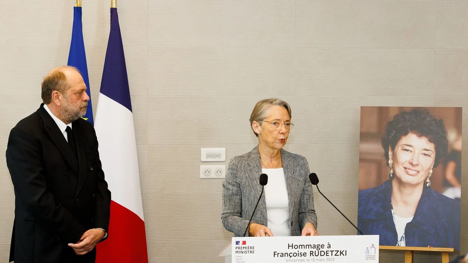 An address at the lectern, in front of the portrait of Françoise Rudetzki and the flags